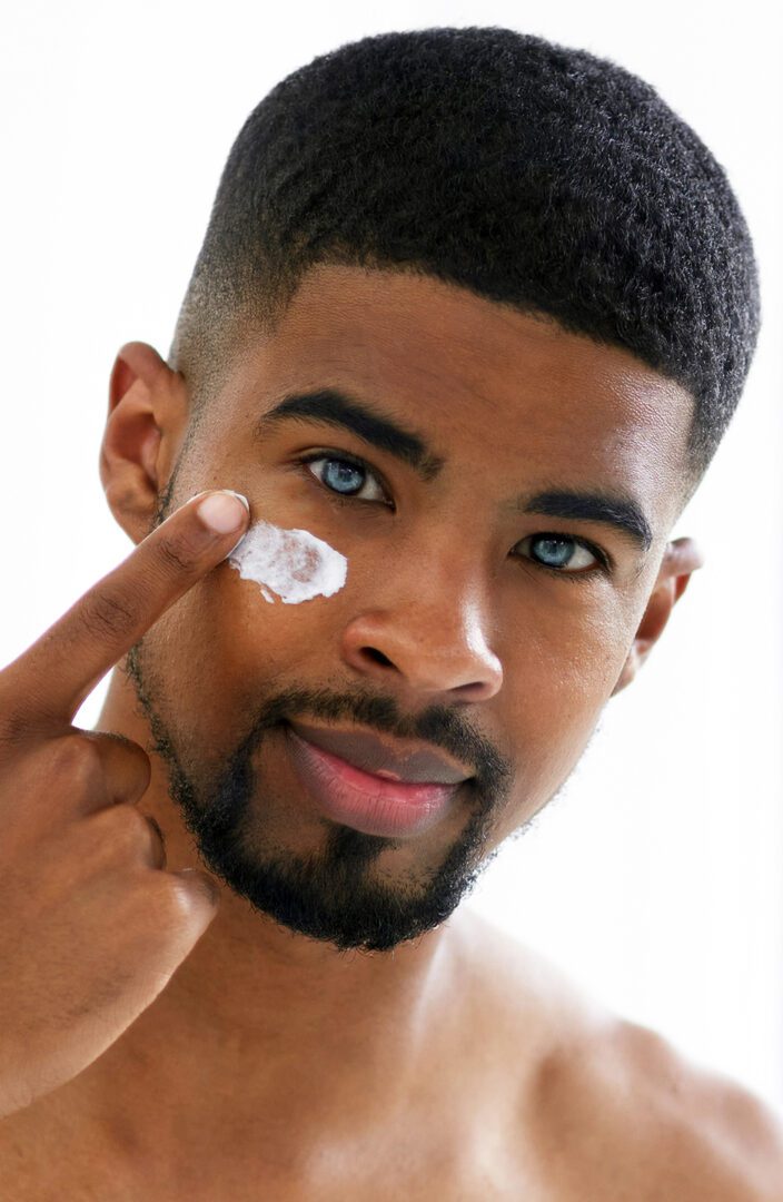 Cropped portrait of a handsome young man standing and using his bathroom mirror to apply moisturizer on his face
