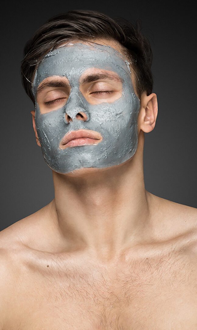 Portrait of a beautiful young man with a facial mud clay mask, face and body skin care treatment.