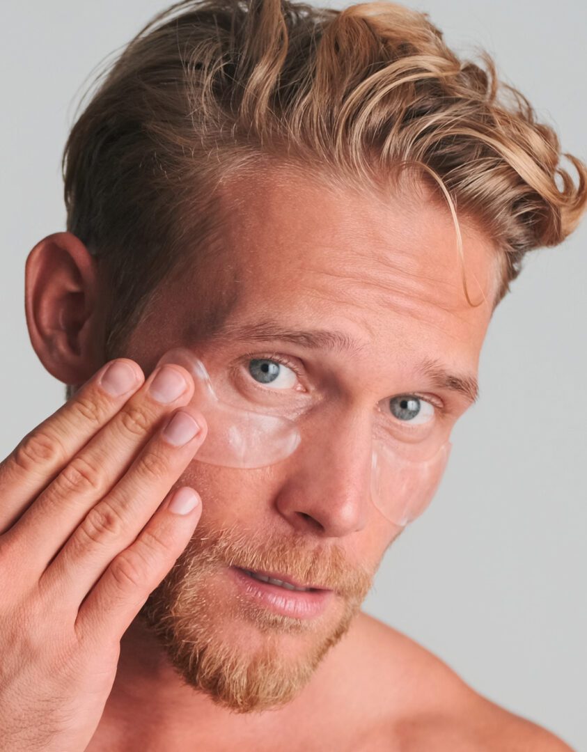 Handsome blond bearded man applying eye patches take care of his skin isolated on white background